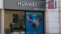 Чоловік зі смартфоном біля табло з індексом Hang Seng у Гонконгу — ілюстративне зображення до новини