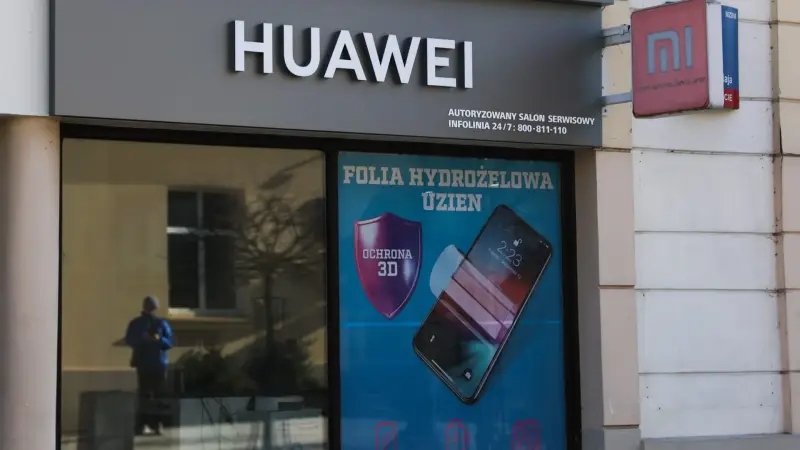 Чоловік зі смартфоном біля табло з індексом Hang Seng у Гонконгу — ілюстративне зображення до новини